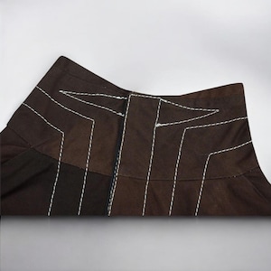 Puede incluir: Primer plano de una prenda marr&oacute;n con costuras blancas. La prenda tiene un dise&ntilde;o geom&eacute;trico con l&iacute;neas verticales y anguladas. La tela parece ser un material de peso medio, posiblemente algod&oacute;n o una mezcla. Las costuras blancas contrastan.