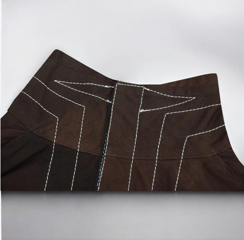 Puede incluir: Primer plano de una prenda marr&oacute;n con costuras blancas. La prenda tiene un dise&ntilde;o geom&eacute;trico con l&iacute;neas verticales y anguladas. La tela parece ser un material de peso medio, posiblemente algod&oacute;n o una mezcla. Las costuras blancas contrastan.