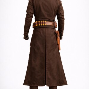 Puede incluir: Un disfraz marr&oacute;n que presenta un abrigo largo, pantalones y una chaqueta de cuello alto. El atuendo incluye un cintur&oacute;n marr&oacute;n con detalles amarillos y una funda. El disfraz est&aacute; dise&ntilde;ado con una est&eacute;tica futurista o de ciencia ficci&oacute;n.
