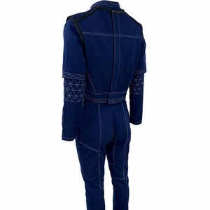 May include: A navy blue jumpsuit with white stitching details. The jumpsuit features a high collar, long sleeves, and a fitted silhouette. The sleeves have a geometric pattern. The back view shows the stitching details and the overall design.