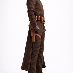 Puede incluir: Traje marr&oacute;n con chaqueta de cuello alto, pantal&oacute;n a juego y botas. El atuendo incluye un cintur&oacute;n con detalles dorados y una funda. La chaqueta y el pantal&oacute;n tienen detalles acolchados.