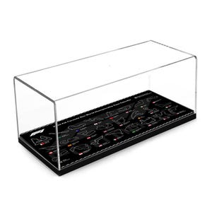 Puede incluir: Una vitrina de acrílico transparente con una base negra. La base presenta un gráfico de los circuitos de Fórmula 1 del calendario de carreras del Campeonato Mundial de la FIA 2024. La caja es rectangular y se encuentra sobre una superficie blanca.