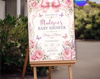 May include: A rectangular baby shower welcome sign on a wooden easel featuring a large pink bow at the top, pink peony floral arrangements, and butterflies. The text reads Welcome to Madison's Baby Shower, Baby in Bloom, May 25, 2026, 2:00 PM.