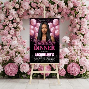 May include: A black sign on a wooden easel, featuring a woman's image and text that reads "Birthday Dinner" and "Jacqueline's 30th Birthday." Pink balloons and floral accents decorate the sign. The background is filled with pink flowers.