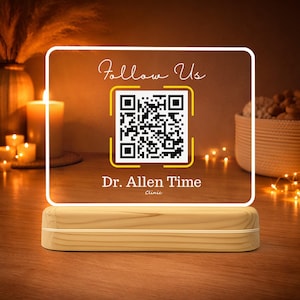 Op de afbeelding: Een verlicht bord met een houten voet toont een QR-code en de tekst "Follow Us" en "Dr. Allen Time Clinic". Het bord gloeit warm, tegen een vage achtergrond met kaarsen en decoratieve elementen.