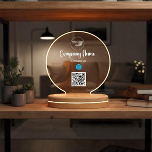 Könnte beinhalten: Ein rundes, beleuchtetes Acrylschild mit Holzsockel. Das Schild zeigt den Text "Your Logo Here", "Company Name" und "Contact us" sowie einen QR-Code. Der Sockel hat ein leuchtendes Licht.