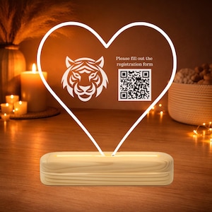 May include: A heart-shaped LED lamp with a tiger head design and the text "Please fill out the registration form" with a QR code. The lamp sits on a wooden base, emitting a warm glow.
