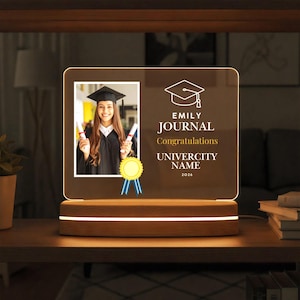 May include: A white ceramic mug with a black handle and the text "But First, Coffee" in a bold, black font. The mug is set against a blurred background, suggesting a cozy setting. The mug appears to be approximately 4 inches tall.