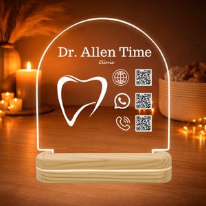 Op de afbeelding: Een verlicht acrylbord met de tekst "Dr. Allen Time Clinic" en een tandafbeelding. Het bord bevat contactpictogrammen en QR-codes, geplaatst op een houten voet. Het bord wordt verlicht met een warme, zachte gloed.