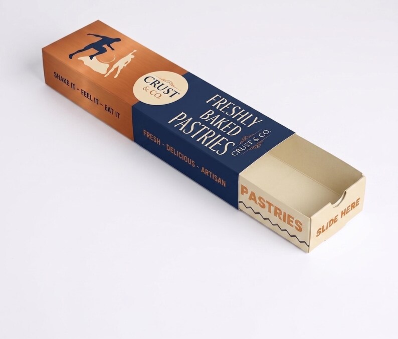 May include: A rectangular cardboard pastry box with a sliding tray. The sleeve is dark blue and copper-colored, featuring the text "CRUST & CO. FRESHLY BAKED PASTRIES," "SHAKE IT - FEEL IT - EAT IT," and "FRESH - DELICIOUS - ARTISAN." The tray says "PASTRIES" and "SLIDE HERE."