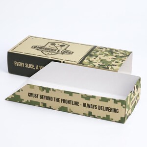 May include: A rectangular cardboard pizza box with a tan and green camouflage pattern. The top features the text COMMANDER'S CRUST and EVERY SLICE, A VICTORY. The side displays the text CRUST BEYOND THE FRONTLINE - ALWAYS DELIVERING.