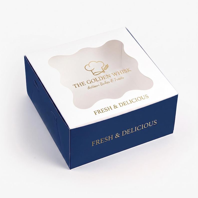 May include: A square cardboard bakery box with a dark blue base and a white lid featuring a wavy transparent window. The lid displays the gold text THE GOLDEN WHISK Artisan Bakes & Treats and FRESH & DELICIOUS, while the side repeats FRESH & DELICIOUS.