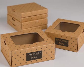 May include: A stack of four brown cardboard boxes and two individual boxes with clear plastic windows. Each box features a repeating dark brown cross pattern and a black rectangular label printed with the text HOME BAKED Enjoy.