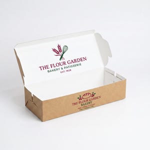 May include: A rectangular cardboard bakery box with a hinged lid, featuring a brown exterior and white interior. The lid displays the logo for The Flour Garden Bakery & Patisserie Est. 1928, while the front panel shows the bakery name and logo.