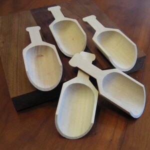 May include: Five wooden scoops, all the same size and shape, are arranged on a wooden surface. The scoops are made of light-colored wood and have a rounded, spoon-like shape.