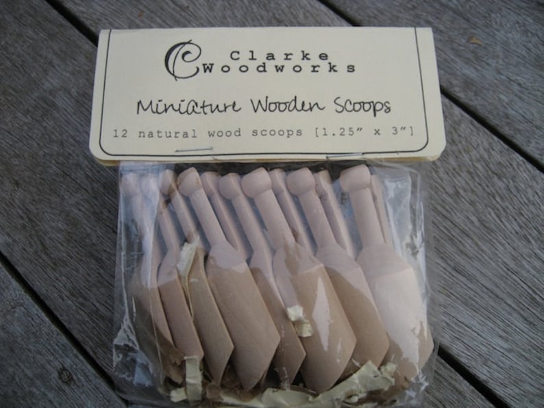 May include: A package of 12 natural wood miniature scoops, measuring 1.25 inches by 3 inches. The scoops are packaged in a clear plastic bag with a brown paper label that reads "Clarke Woodworks Miniature Wooden Scoops".