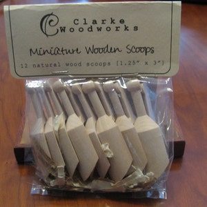 May include: A package of 12 natural wood miniature scoops, each measuring 1.25 inches by 3 inches. The scoops are packaged in a clear plastic bag with a brown paper label that reads "Clarke Woodworks Miniature Wooden Scoops".