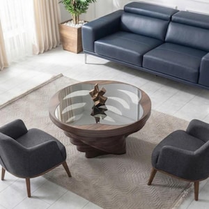 May include: An aerial view of a contemporary living room. A navy blue leather sofa is positioned against a wall, with a round coffee table and two grey armchairs in front. The coffee table has a glass top and a wooden base.