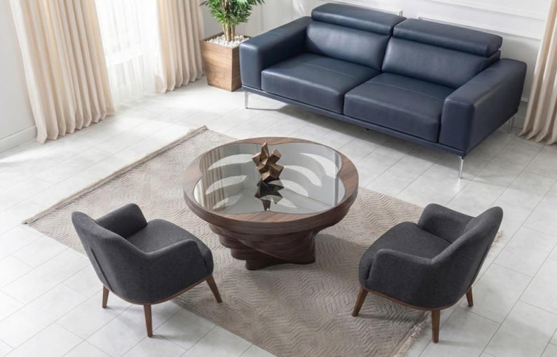May include: An aerial view of a contemporary living room. A navy blue leather sofa is positioned against a wall, with a round coffee table and two grey armchairs in front. The coffee table has a glass top and a wooden base.
