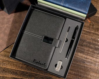 May include: A black leather journal and pen set in a gift box. The journal has a silver clasp and the name "Robert" is inscribed on the cover. A silver pen and a black pen are included.