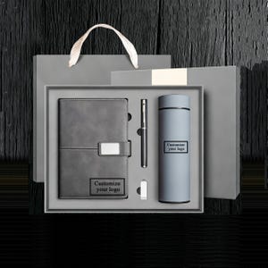 Könnte beinhalten: Ein graues Geschenkset mit Notizbuch, Stift, Wasserflasche und USB-Stick. Das Notizbuch hat einen Verschluss und den Text "Customize your logo". Die Wasserflasche trägt ebenfalls den Text "Customize your logo". Das Set wird in einer grauen Box mit Griff präsentiert.