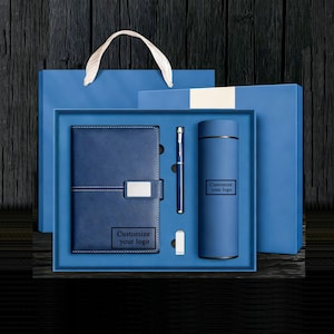 Puede incluir: Un juego de regalo azul que incluye un cuaderno, un bolígrafo, un vaso y una unidad USB. El cuaderno tiene un cierre plateado y el texto "Customize your logo". El vaso también tiene el texto "Customize your logo". El juego se presenta en una caja de regalo azul con una bolsa a juego.