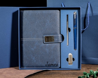 May include: A blue leather journal and pen set presented in a gift box. The journal has a clasp and the name "James" is embossed on the cover. A blue pen, a silver pen, and a silver pen clip are included.