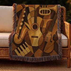 May include: A woven throw blanket featuring a geometric design of musical instruments in shades of brown, tan, and gold. The instruments include a saxophone, guitar, trumpet, piano keys, and a violin. The blanket has a fringed edge and is draped over a wicker chair.
