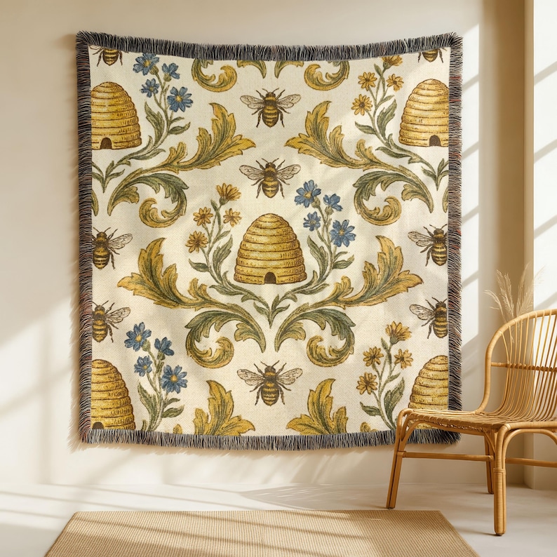 May include: A woven throw blanket featuring a repeating pattern of bees, beehives, and floral designs in yellow, blue, and green on an off-white backdrop. The blanket has a fringed edge and is displayed on a wall.