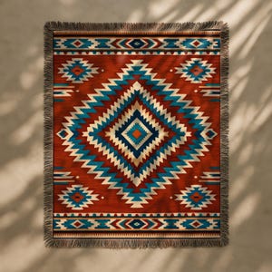 May include: A woven throw blanket with a geometric pattern in shades of red, teal, and cream. The design features diamond and zigzag shapes. The blanket has a fringed edge and is suitable for home decor.