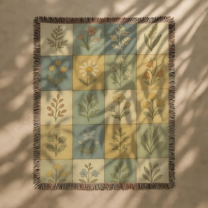 May include: A woven throw blanket with a floral pattern. The blanket features a grid of squares in pastel yellow and blue, each containing a different botanical illustration. The edges are finished with a fringed border.