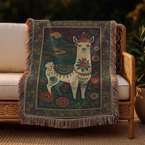 Op de afbeelding: Een geweven sprei met een gedetailleerde illustratie van een lama versierd met bloemaccenten. Het ontwerp omvat een berglandschap, een zon en een decoratieve bloemenrand in groen, bordeauxrood en crème. De sprei heeft een gefranjerde rand.
