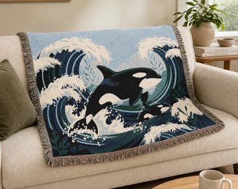 May include: A woven throw blanket featuring a large black and white orca whale leaping through stylised dark blue and white ocean waves. The rectangular blanket has a fringed edge and displays a detailed graphic design of marine life.