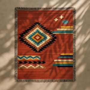 Könnte beinhalten: Eine rechteckige gewebte Wurkdecke mit einem geometrischen Muster in Rot-, Schwarz-, Gelb-, Blau- und Weißtönen. Die Decke hat einen Fransenrand und ein südwestliches Design.
