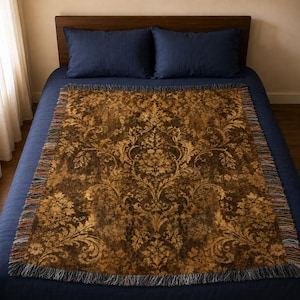 May include: A rectangular woven throw blanket featuring a dark brown and gold damask pattern with intricate floral and scrollwork motifs. The blanket has a fringed edge with multi-colored threads visible along the sides and bottom borders.