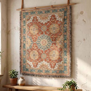 May include: A rectangular woven wall tapestry featuring a central teal mandala pattern surrounded by intricate floral motifs in shades of rust orange, cream, and muted blue. The textile has a fringed border and hangs from a wooden rod.