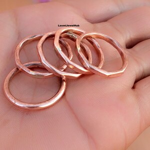 May include: A set of four copper-colored rings with a faceted, multi-sided exterior surface. The rings have a metallic finish and are arranged in a cluster. The text LaxmiJewelHub is printed in small black letters near the center of the rings.