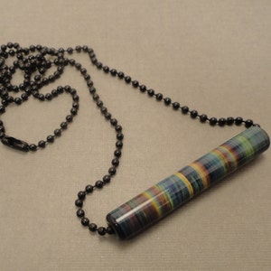 May include: A colorful glass pendant with a striped pattern hangs from a black beaded chain. The pendant is cylindrical in shape and has a variety of colors, including blue, green, yellow, and red.
