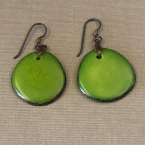 May include: A pair of green oval-shaped earrings with a dark brown border. The earrings are made of natural materials and have a simple, elegant design.