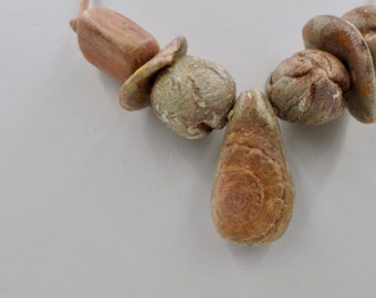 May include: A necklace made of brown and green stone beads. The beads are irregular in shape and have a rough texture. The necklace is strung on a brown cord.