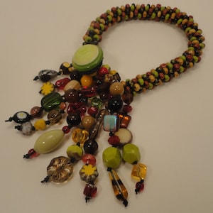 May include: A multi-colored beaded necklace with a green button and a long tassel of various beads in shades of brown, green, red, and yellow.