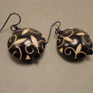 May include: Black and white dangle earrings with a floral design. The earrings are made of metal and have a black finish. The floral design is white and gold.