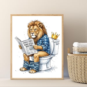 May include: A framed art print featuring a lion sitting on a toilet, wearing a blue plaid shirt and reading a newspaper. The newspaper headline reads "Jungle Times: King Still Waiting." A gold crown sits on the toilet tank.
