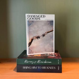 May include: A stack of three books with different covers. The top book is titled "DAMAGED GOODS" with an image of two hands reaching out. Below it is a book with "Rosemary for Remembrance" and the bottom book reads "BRING HIM TO HIS KNEES".