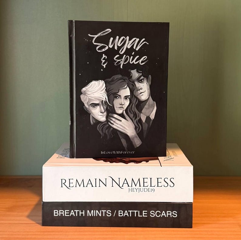 May include: A stack of three books. The top book is black with the title "Sugar & Spice" in white script and illustrations of three people. The middle book is white with "REMAIN NAMELESS" printed on it. The bottom book is black with "BREATH MINTS / BATTLE SCARS".