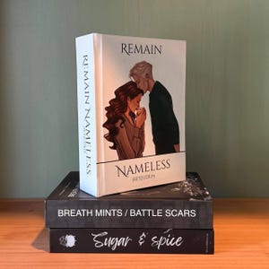 May include: A stack of three books. The top book is titled "Remain Nameless" with an illustration of a couple. The spine reads "Remain Nameless Heyjude19". Below it is a book titled "Breath Mints / Battle Scars". The bottom book is titled "Sugar & Spice".