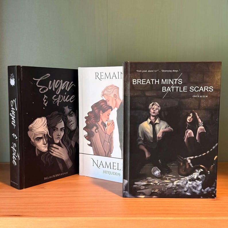 May include: Three hardcover books with illustrated covers. The first book is black with the title "Sugar & Spice" and a drawing of three people. The second book is white with the title "Remain" and a couple. The third book is dark with the title "Breath Mints Battle Scars".