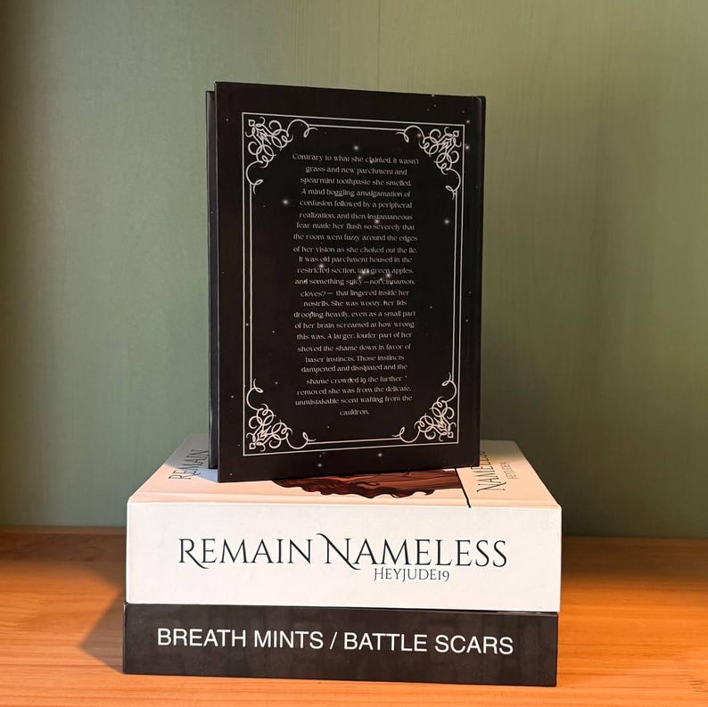 May include: Three books stacked on top of each other. The top book has a black cover with white text and a decorative border. The middle book is white with the title "REMAIN NAMELESS" and the author's name. The bottom book is black with the title "BREATH MINTS / BATTLE SCARS".