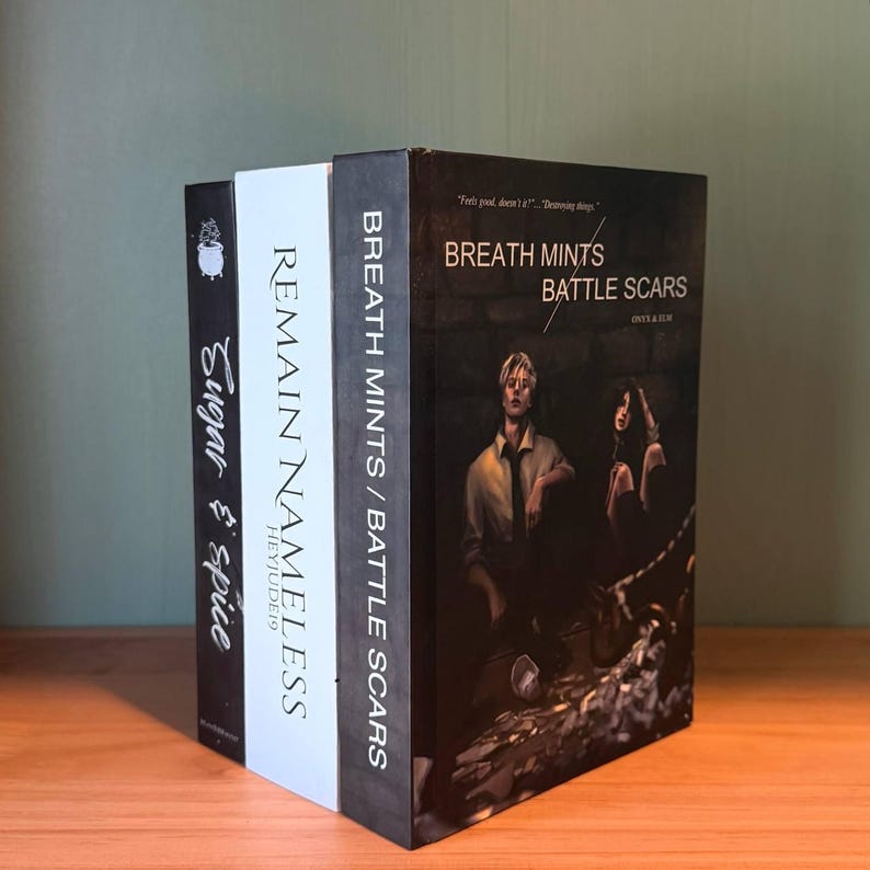May include: Three decorative books with titles: "Sugar & Spice", "Remain Nameless", and "Breath Mints / Battle Scars". The books are black, white, and black, respectively. The "Breath Mints / Battle Scars" book features a photo of two people.