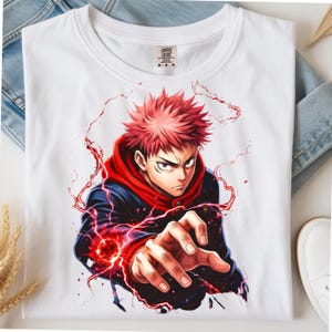 以下が含まれることがあります： 赤いスパイクヘアのアニメキャラクターが描かれた白いTシャツ。赤いフード付きのダークジャケットを着用し、片手を前に突き出している。キャラクターの周囲には赤いエネルギーエフェクトと稲妻のような筋が描かれている。
